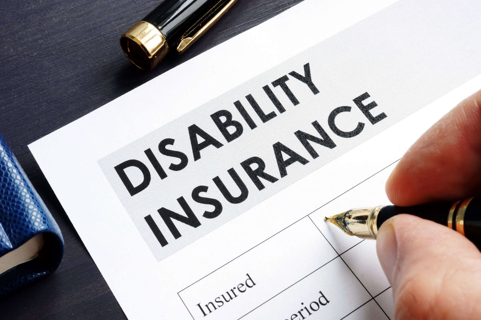 Close-up of a hand filling in a form labeled Disability Insurance; weighing private disability vs. Social Security benefits.