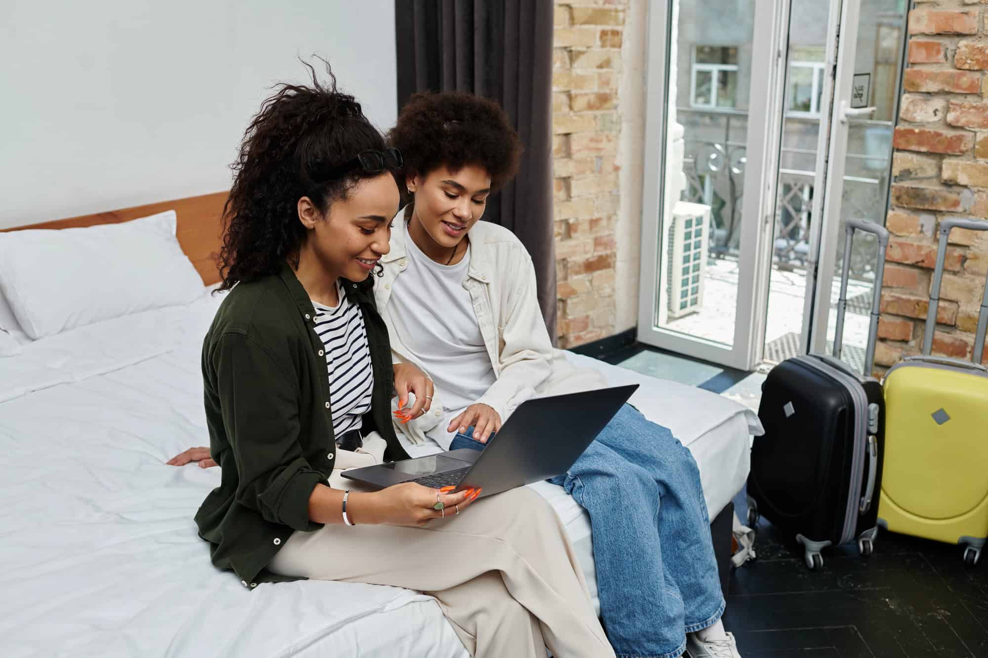 A couple seated on the edge of a bed, looking at a laptop computer screen together; traveling while on long-term disability requires careful preparation.