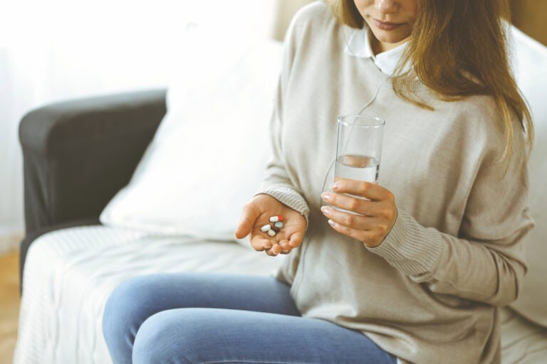 A woman considering her pre-existing conditions’ impact on LTD eligibility while she takes pills and a glass of water sitting down.