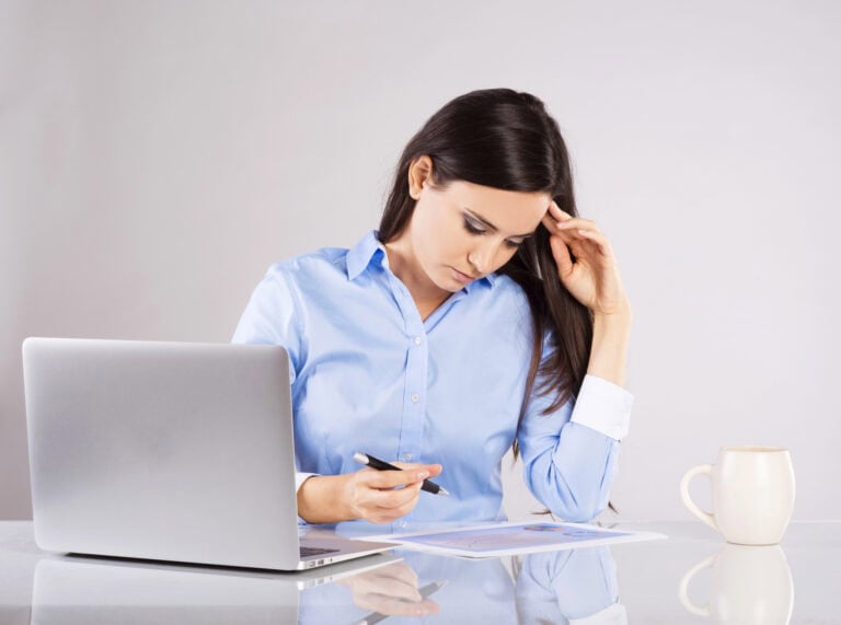 Young woman preparing a printed tax worksheet at a desk with a cup of coffee and an open laptop computer; reviewing the tax implications of LTD benefits.