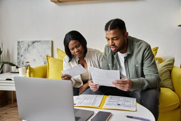 Young couple seated on a couch, reviewing documents from multiple sources; coordinating LTD with Social Security benefits.