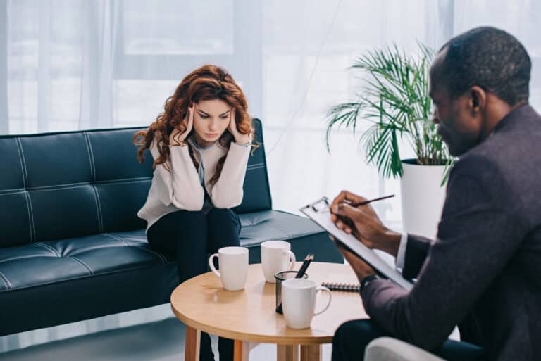 Young woman on sofa in psychiatrist’s office, undergoing mental health assessment; establishing mental health qualifications for LTD.