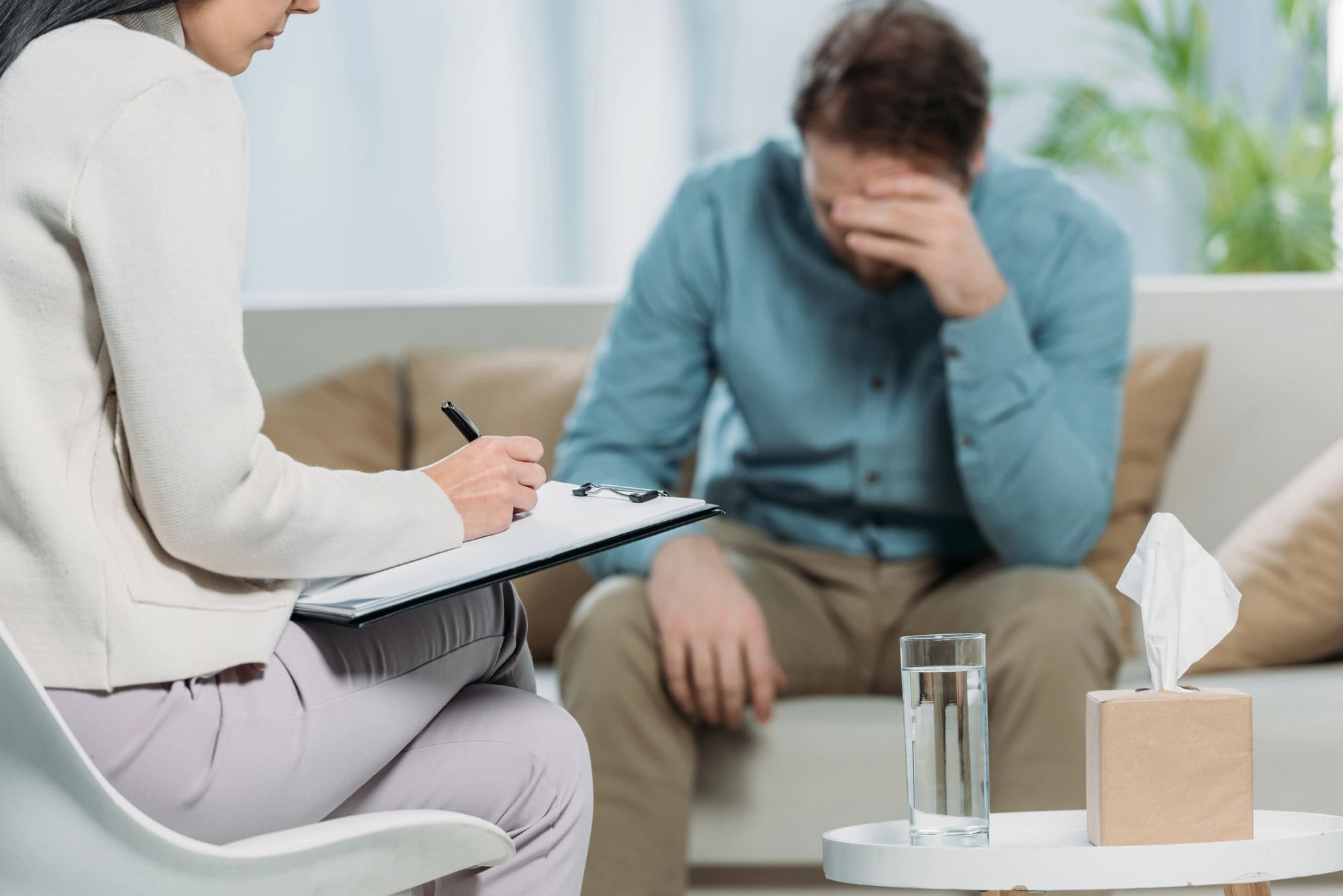 The mental health impact on LTD claims can be significant. A man sitting on a sofa in a therapist’s office, resting his head on one hand while the therapist takes notes.