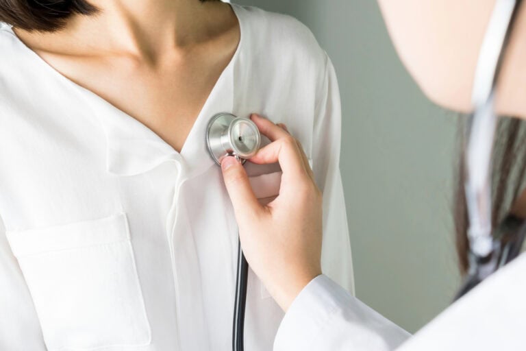 A physician listening to a patient’s chest through a stethoscope during a doctor visit for long-term disability claim.