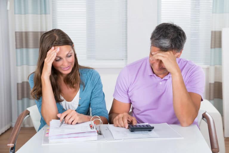 Married couple reviewing financial obligations using a calculated and a binder full of printed documents; planning how to manage LTD benefits in bankruptcy filing.