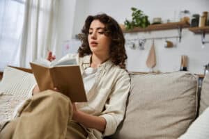A woman seated on a sofa, writing an entry in a cloth-bound journal; keeping a symptom log can be useful in overcoming LTD documentation hurdles.