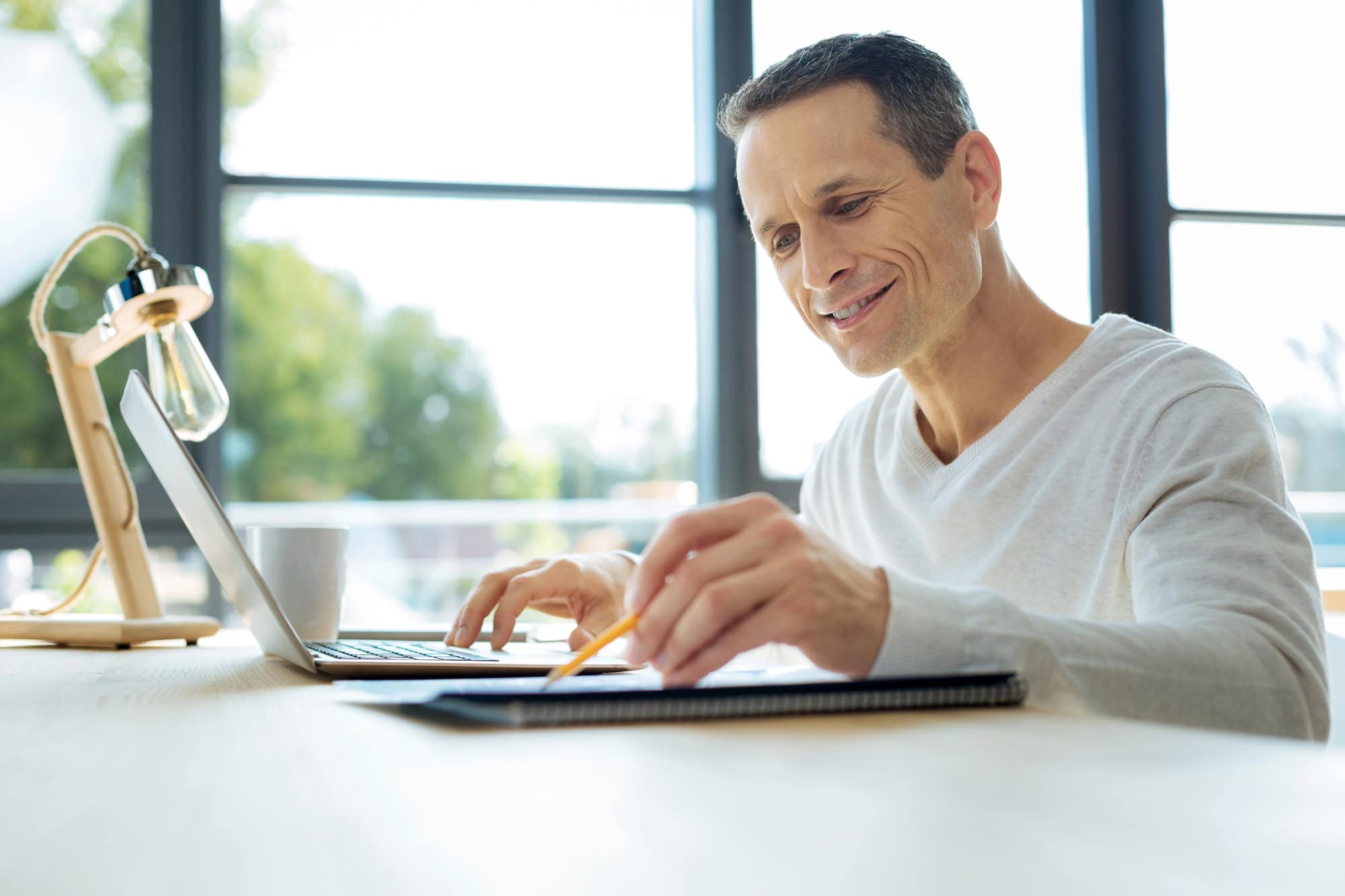Middle-aged man seated at a desk, using a set of paper documents and a laptop computer to conduct a short-term vs. long-term disability insurance comparison.
