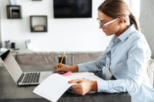 A woman reviewing a set of records in a home office with a laptop computer and a cup of coffee; understanding LTD claim review process to prepare.