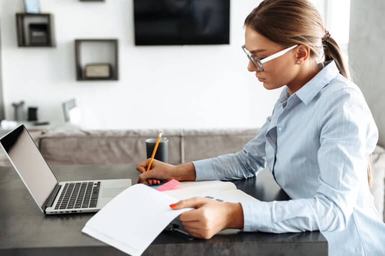 A woman reviewing a set of records in a home office with a laptop computer and a cup of coffee; understanding LTD claim review process to prepare.