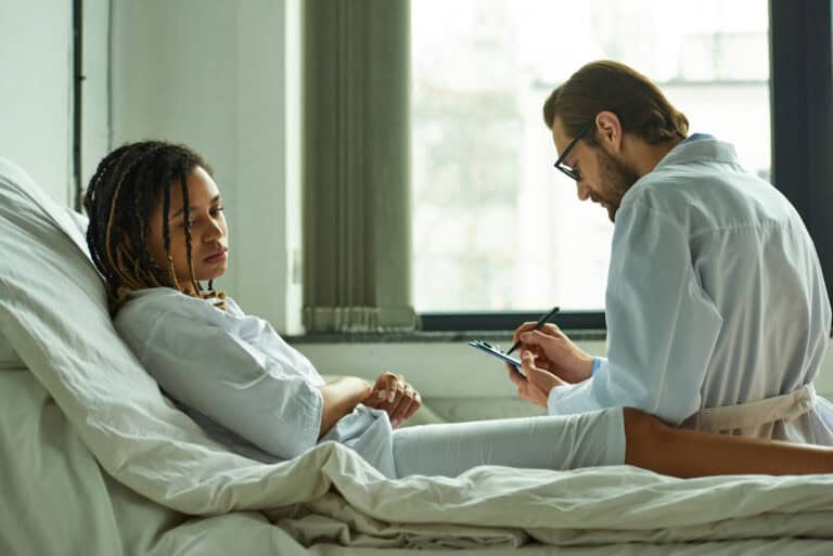 Young woman in hospital bed, receiving medical assessment from a physician; common conditions qualifying for LTD.