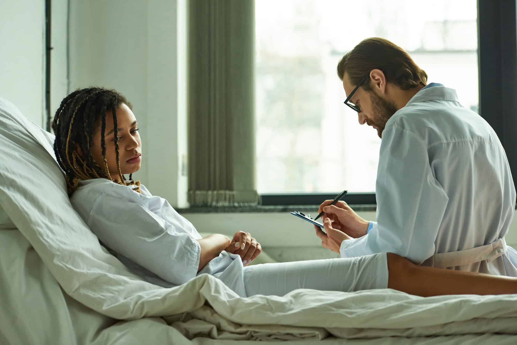 Young woman in hospital bed, receiving medical assessment from a physician; common conditions qualifying for LTD.