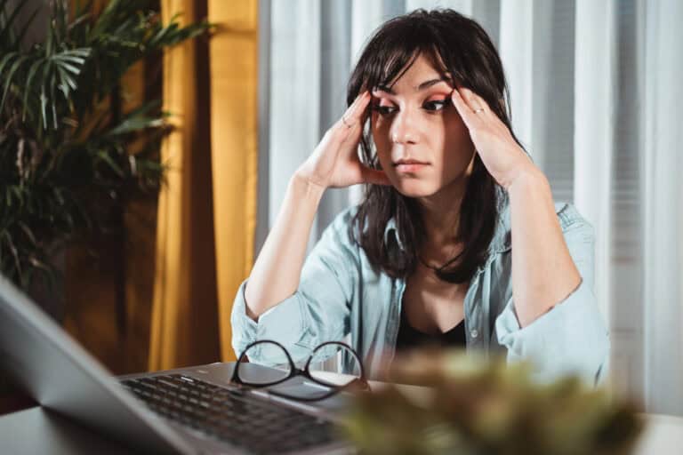 Young disabled woman rubbing her temples as she stares at a laptop computer screen in a home setting; wondering “Can LTD benefits be garnished by creditors?