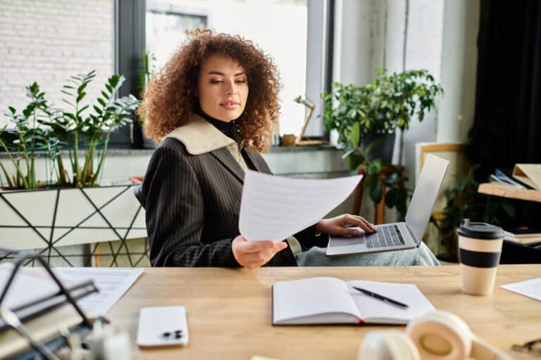 A woman seated in a home office, comparing a printed policy document to her laptop computer screen; planning for seamless transition STD to LTD benefits.