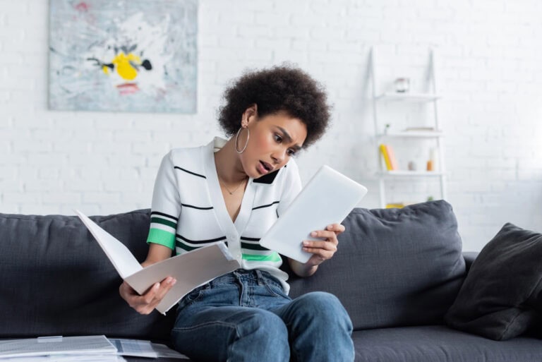 A young woman balancing a phone between her shoulder and ear examines a notebook in one hand while holding a folder of documents open in the other; following a guide to appealing LTD denial.