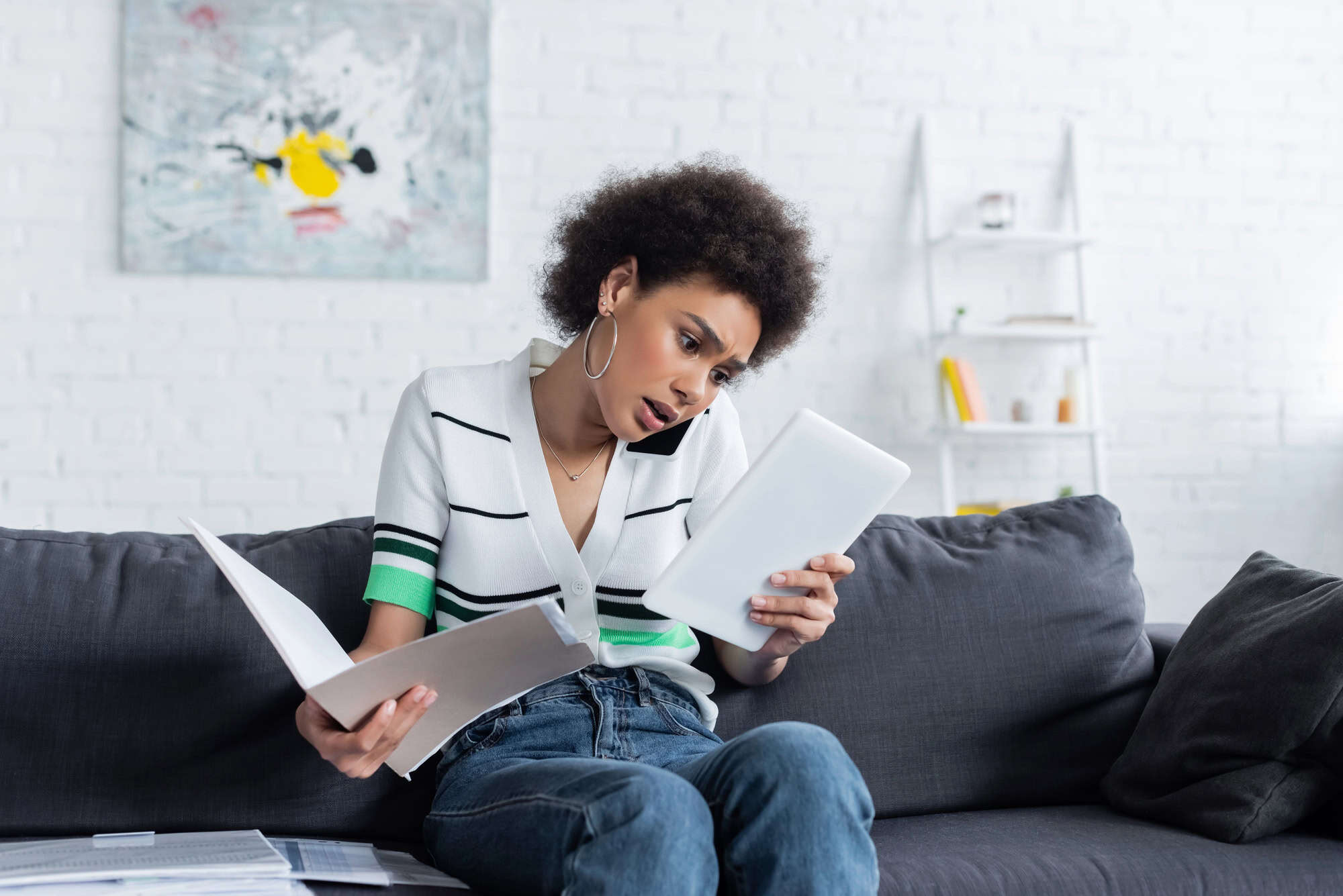 A young woman balancing a phone between her shoulder and ear examines a notebook in one hand while holding a folder of documents open in the other; following a guide to appealing LTD denial.